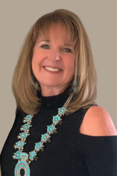 Headshot of Sally Taggart, a professional life coach, author, and speaker, smiling warmly. She is wearing a black top with open shoulders and a striking turquoise and silver necklace, reflecting her confident and approachable personality.